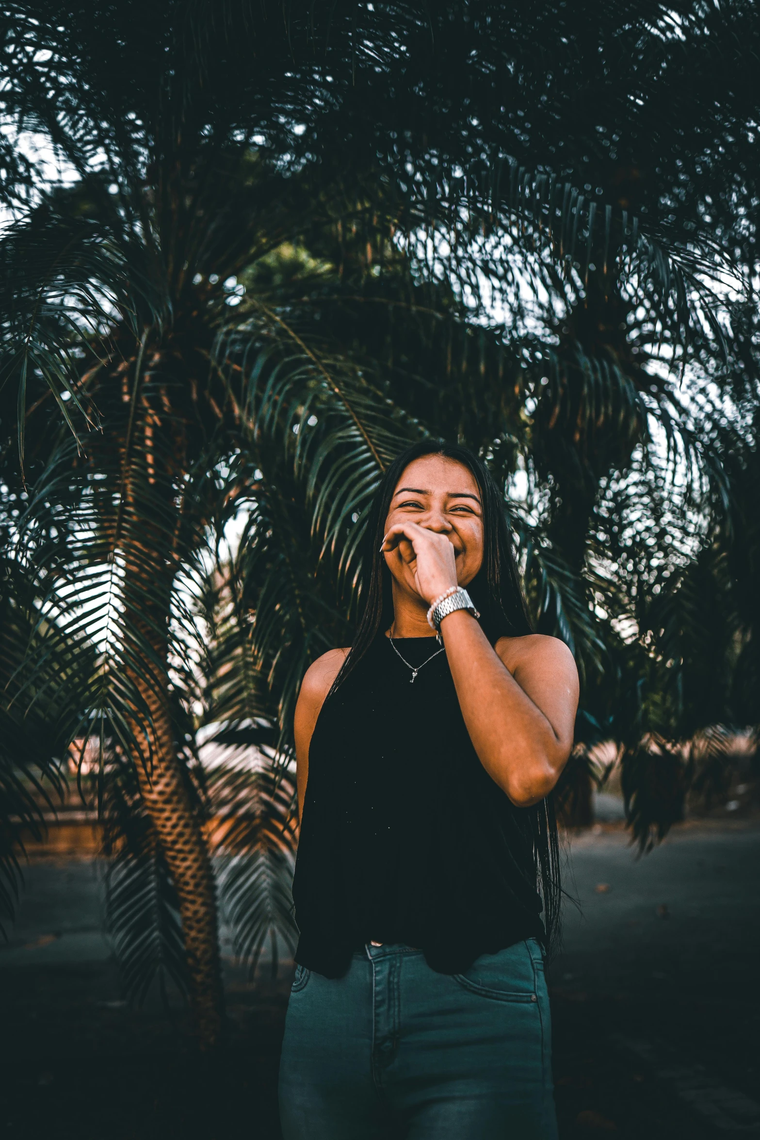 a woman standing in front of a palm tree talking on a cell phone, pexels contest winner, happening, fleshy creature above her mouth, wearing a cropped black tank top, woman in streetwear, crying and smiling franticly