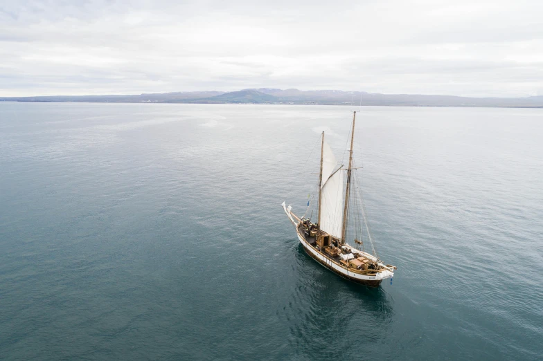 a sailboat in the middle of a large body of water, kahikatea, wooden boat, looking down on the camera, ignant