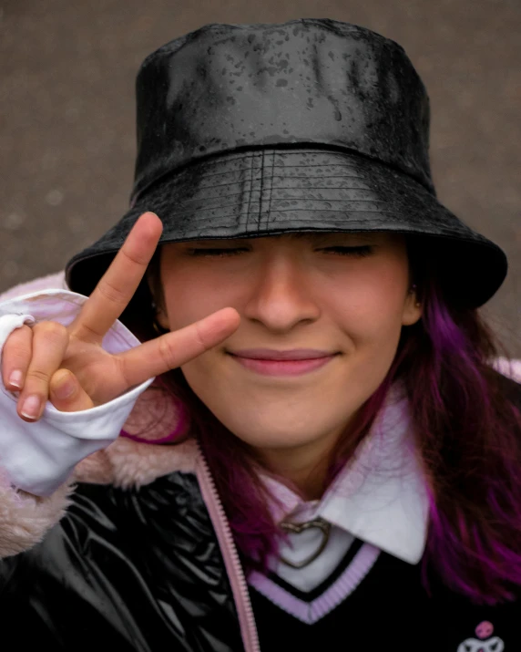 a woman in a black hat making a peace sign, inspired by Ion Andreescu, trending on pexels, lgbt, bucket hat, 33mm photo