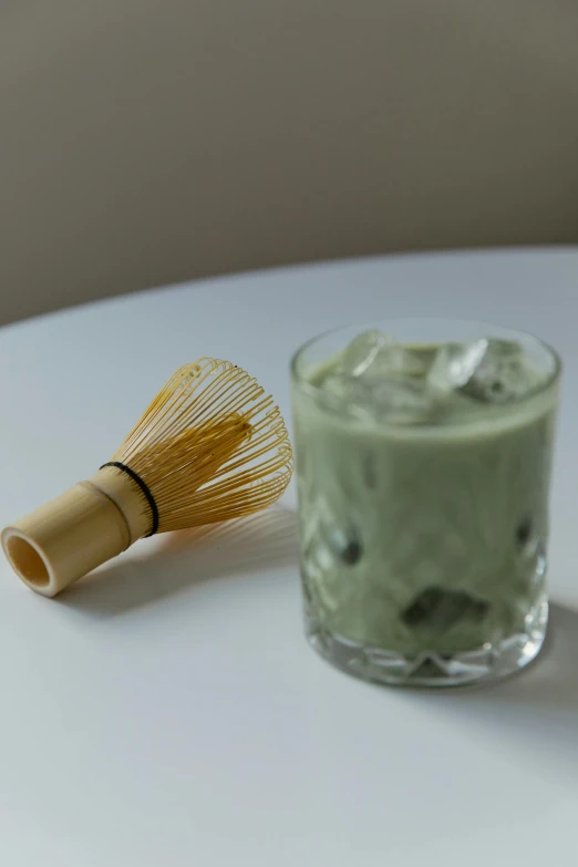 a cup of matcha and a whisk on a table, inspired by Kanō Shōsenin, sōsaku hanga, iced tea glass, creamy skin, bamboo, product shot