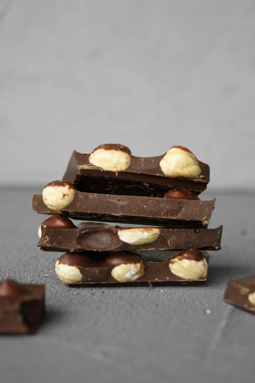 a stack of pieces of chocolate with nuts on top, buzzed sides, in a row, no crop, black rococo