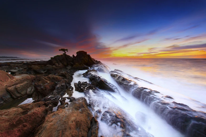 a large body of water sitting on top of a rocky beach, a picture, inspired by Michael Komarck, unsplash contest winner, water flow, indonesia national geographic, california coast, ultrawide lens”