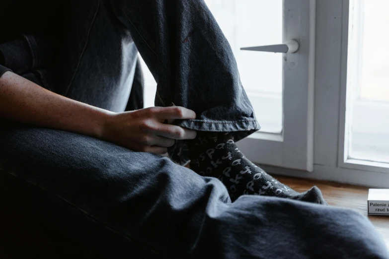 a person sitting on the floor in front of a window, by Nina Hamnett, trending on pexels, denim, gnarly details soft light, wearing black, wearing pajamas