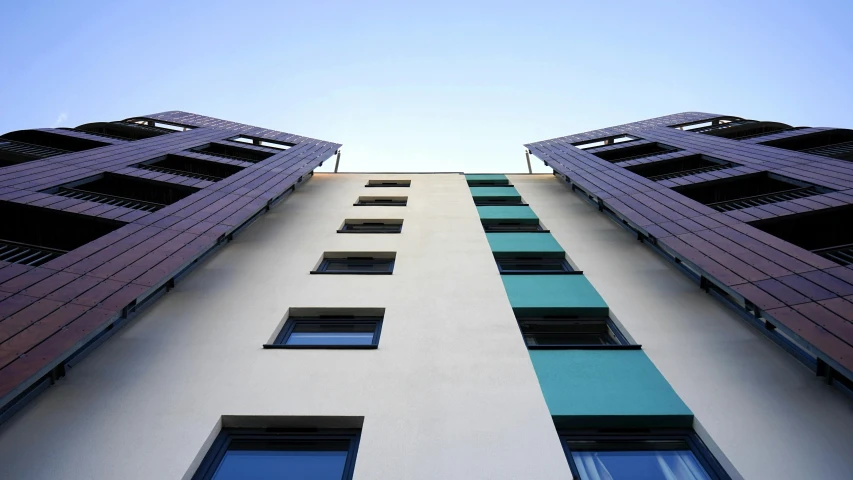 a tall building with multiple windows in front of a blue sky, inspired by Richard Wilson, unsplash, minimalism, coventry city centre, wooden buildings, looking upwards, teal sky