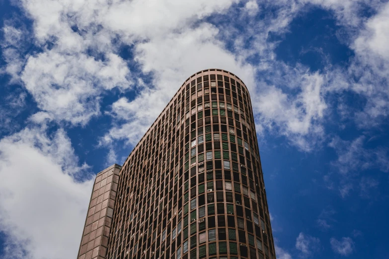 a tall building with a blue sky in the background, by Lee Loughridge, unsplash, brutalism, curved, brown, cloud palace, 90s photo