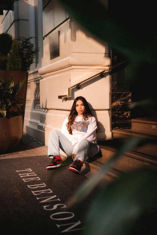 a woman sitting on the ground in front of a building, an album cover, inspired by Elsa Bleda, trending on pexels, graffiti, wearing a white sweater, red shoes, madison beer girl portrait, portrait pose
