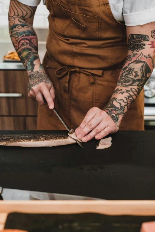 a man in an apron preparing food in a kitchen, a tattoo, trending on pexels, fish skin, smoked layered, carving, long