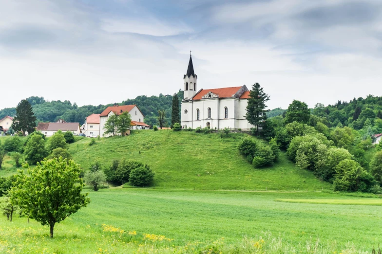 a church sitting on top of a lush green hillside, inspired by Jan Kupecký, pexels contest winner, white buildings with red roofs, in a large grassy green field, villany, conde nast traveler photo