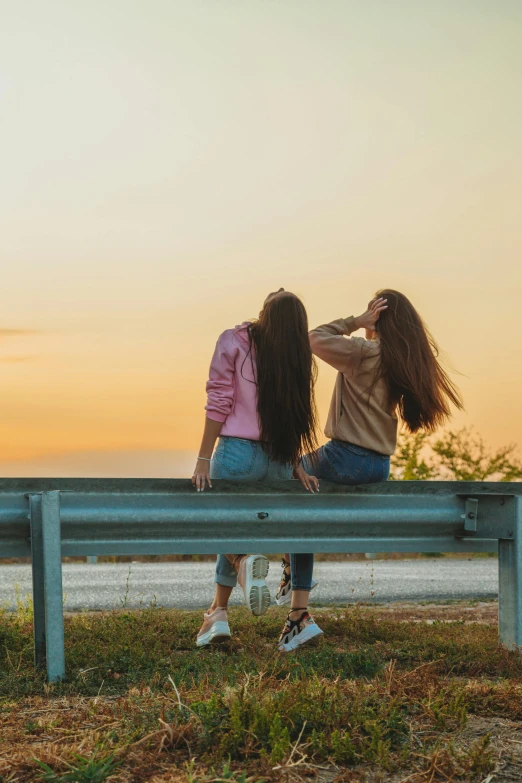 a couple of women sitting on top of a wooden bench, a picture, trending on pexels, long flat hair, at dusk at golden hour, teenager, road trip