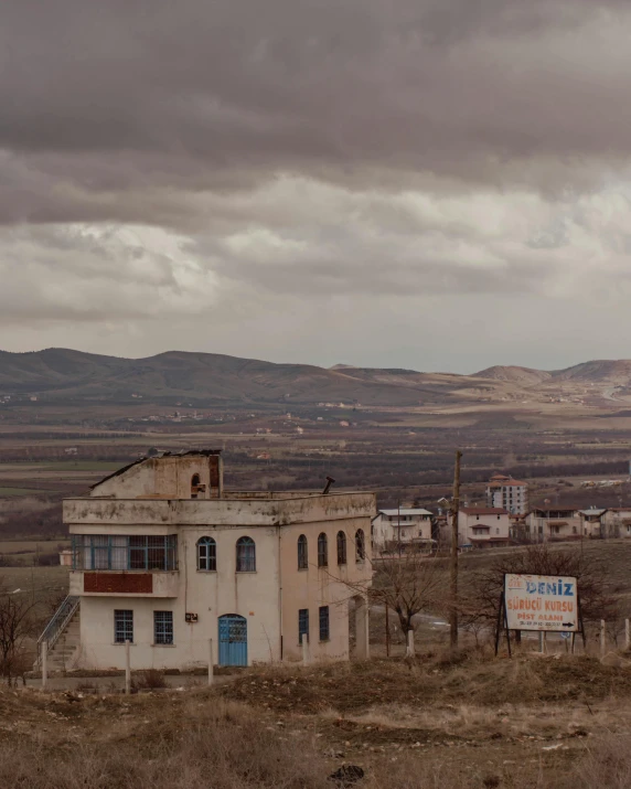 an old building sitting in the middle of a field, unsplash contest winner, distant town in valley and hills, ayanamikodon and irakli nadar, grey skies with two rainbows, soviet town