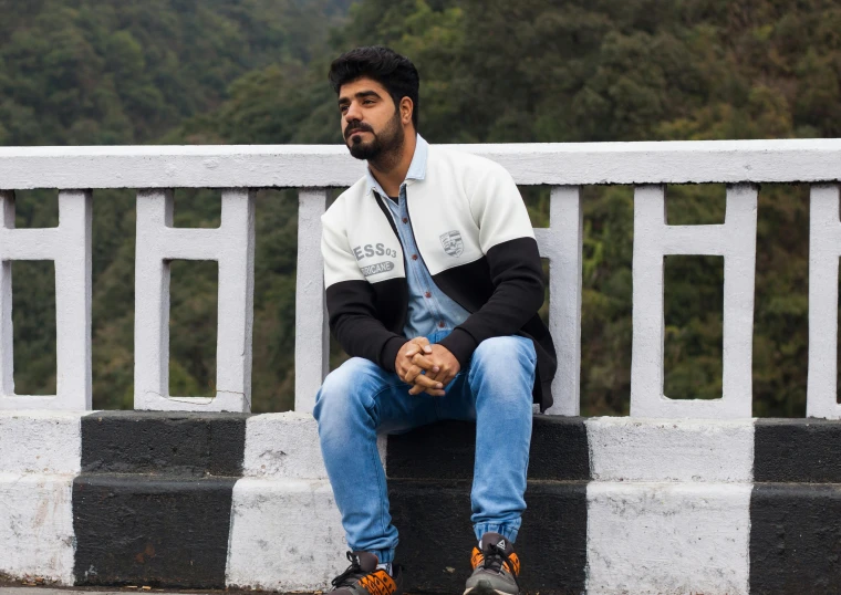 a man sitting on the edge of a bridge, an album cover, inspired by Saurabh Jethani, pexels contest winner, a portrait of rahul kohli, casual streetwear, standing on mountain, off - white collection