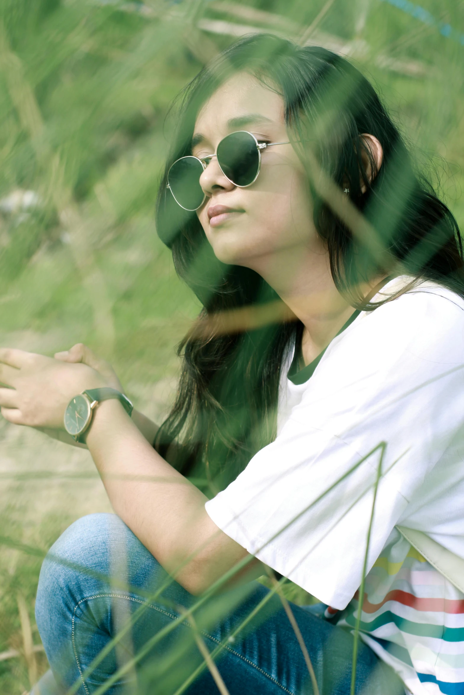 a woman sitting on top of a grass covered field, a picture, inspired by Bernardino Mei, unsplash, sumatraism, wear ray - ban glass, watch photo, wearing casual clothing, greenish tinge