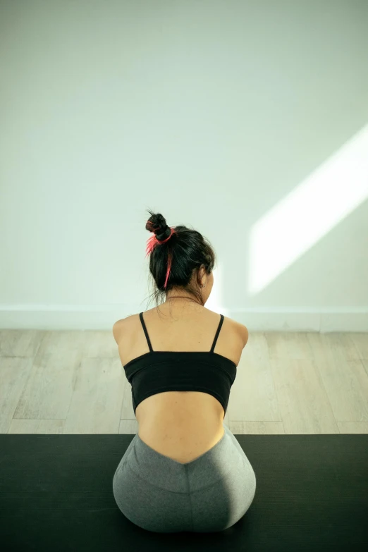 a woman sitting on a yoga mat in a room, showing her shoulder from back, louise zhang, backlite, shy looking down