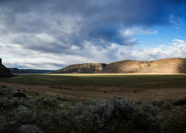 a wide open field with mountains in the background, by Hallsteinn Sigurðsson, unsplash contest winner, land art, mesa plateau, low key light, panoramic, in between a gorge