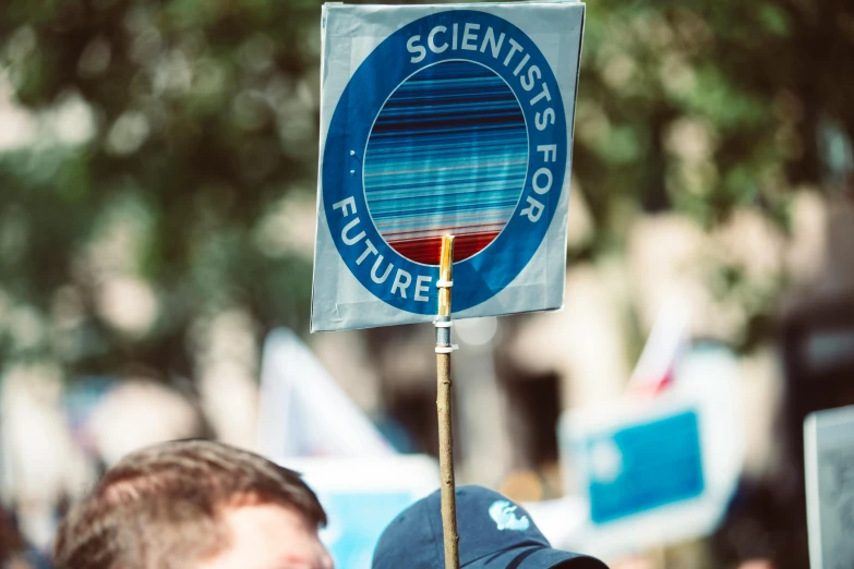 a close up of a person holding a sign, shutterstock, excessivism, scientists, bright blue future, paul davey, photographed from the back