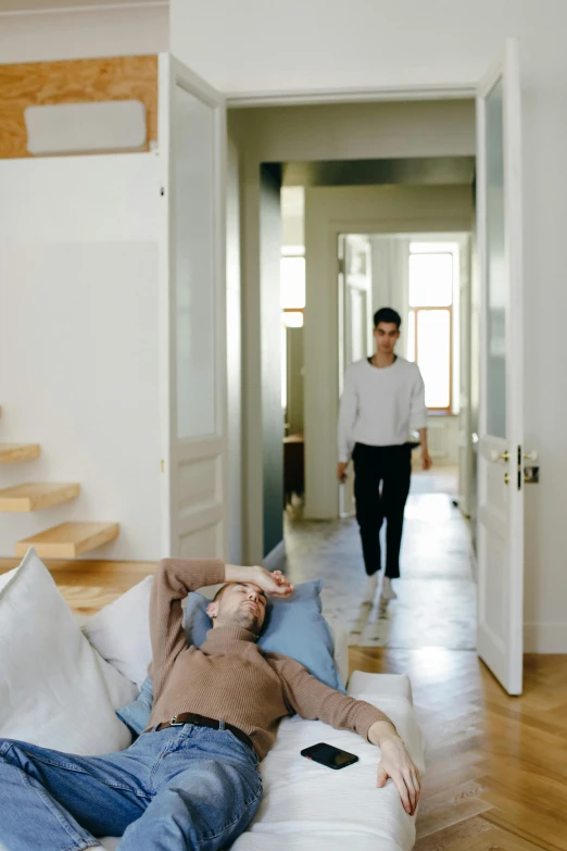 a man laying on a couch in a living room, by Nina Hamnett, visual art, apartment hallway, two people, walking away, promo still