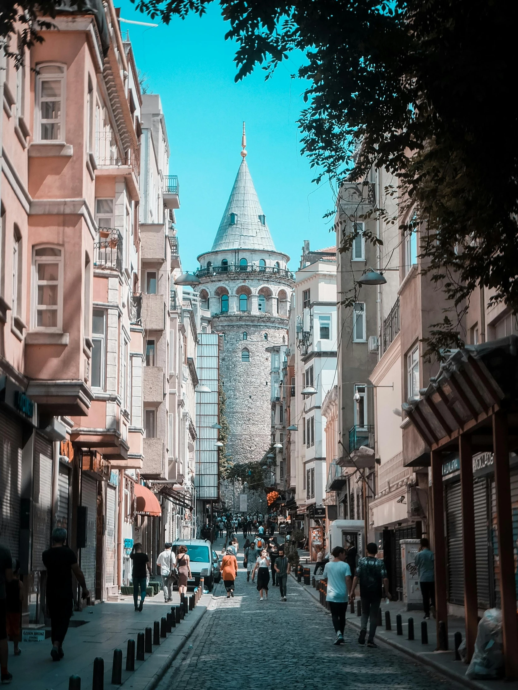 a group of people walking down a street next to tall buildings, a photo, pexels contest winner, art nouveau, mixture turkish and russian, turrets, 🚿🗝📝, street of teal stone