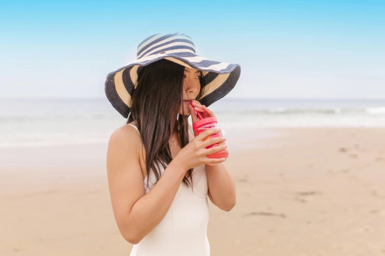 a woman standing on top of a sandy beach, drinking a strawberry iced latte, red hat, avatar image, skincare