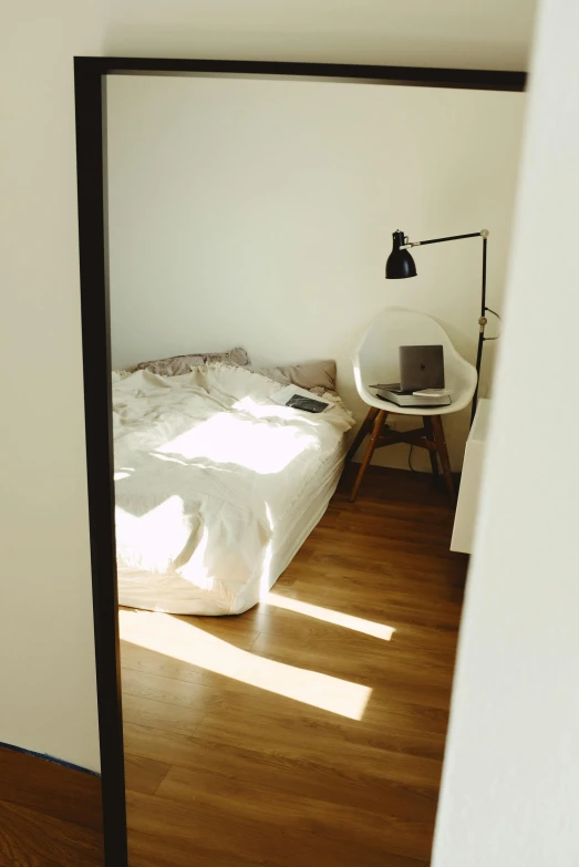 a bed sitting in a bedroom next to a mirror, by Niko Henrichon, unsplash, light and space, sun lighting from above, home office, sparse room, small bed not made