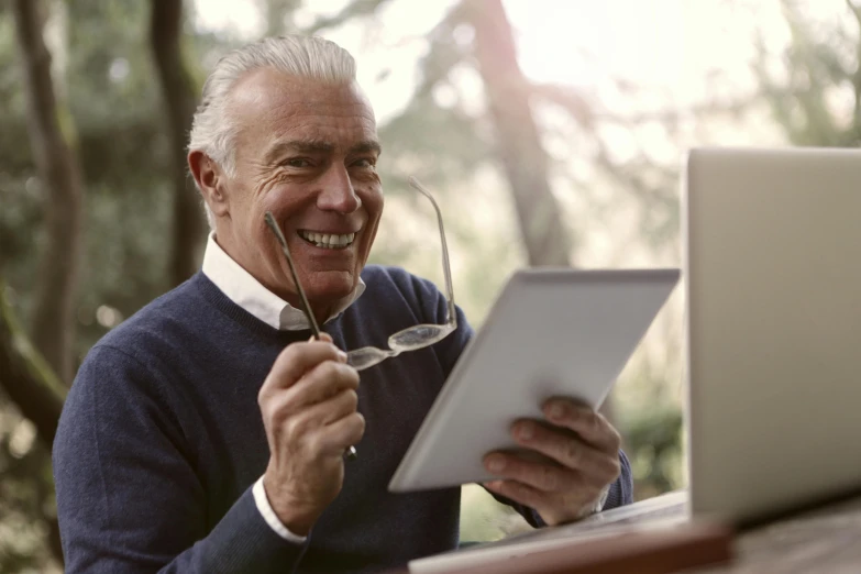 a man sitting at a table with a laptop and a pair of glasses, pexels contest winner, a silver haired mad, reading under a tree, a still of a happy, healthcare