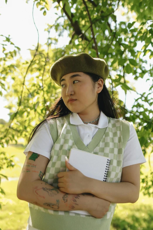 a woman standing under a tree holding a book, an album cover, inspired by Jung Park, unsplash, wearing a vest, wearing a beret, casual green clothing, ((portrait))