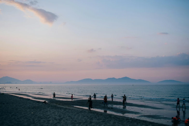 a group of people standing on top of a sandy beach, unsplash contest winner, vietnam, early evening, sparsely populated, pink skies