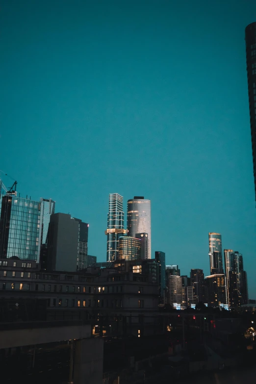 the city skyline is lit up at night, pexels contest winner, tall minimalist skyscrapers, melbourne, blue and clear sky, low quality photo