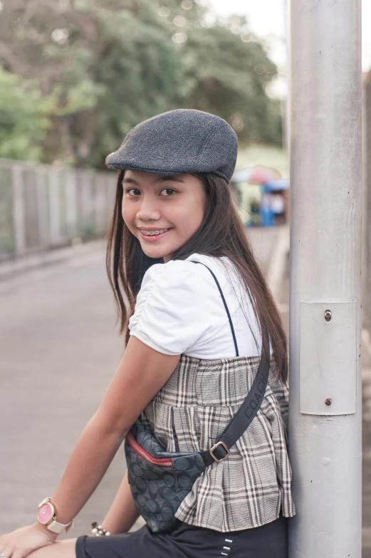 a woman leaning against a pole with a hat on, inspired by Oka Yasutomo, unsplash, dressed as schoolgirl, 🤤 girl portrait, grey, small in size