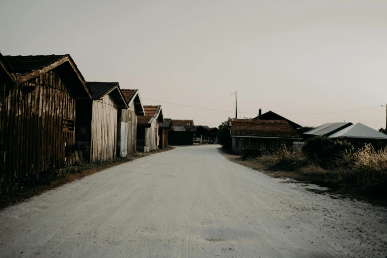 a dirt road lined with old wooden buildings, by Christen Dalsgaard, postminimalism, early evening, high quality photos, grey, brown