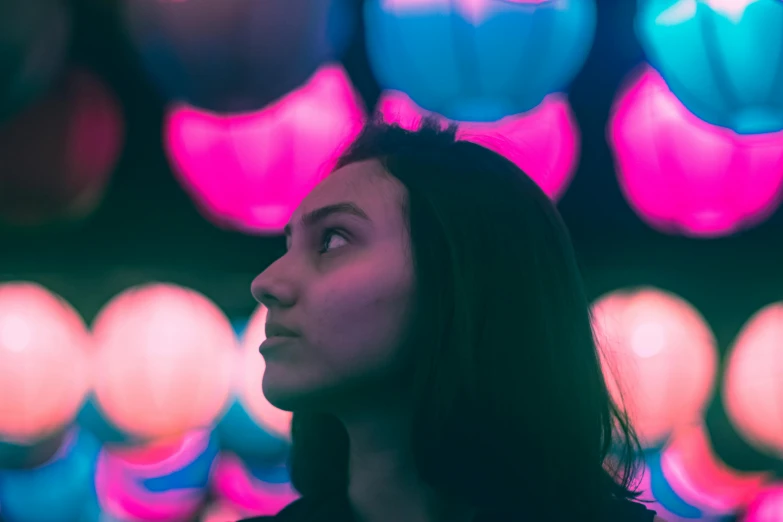 a woman standing in front of a bunch of balloons, by Adam Marczyński, pexels contest winner, synchromism, violet and aqua neon lights, close - up profile face, young woman looking up, lines of lights