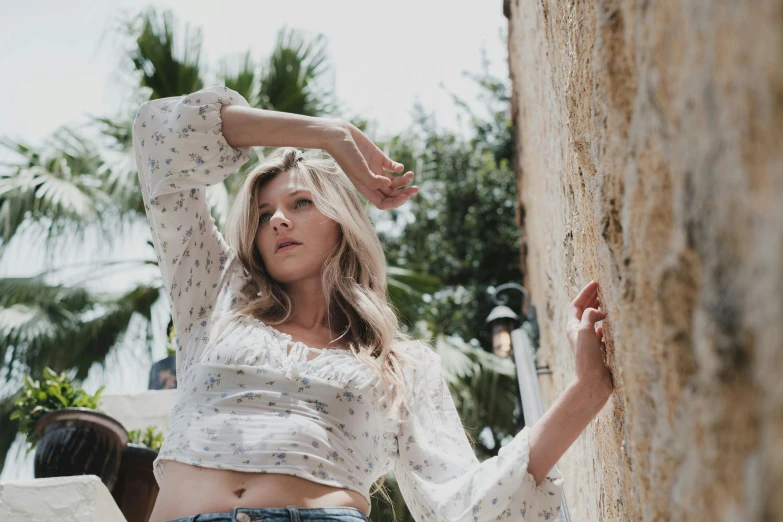a woman leaning against a wall with her hands on her head, trending on pexels, renaissance, loose - fitting blouses, jaina proudmoore, wearing a sexy cropped top, tourist photo