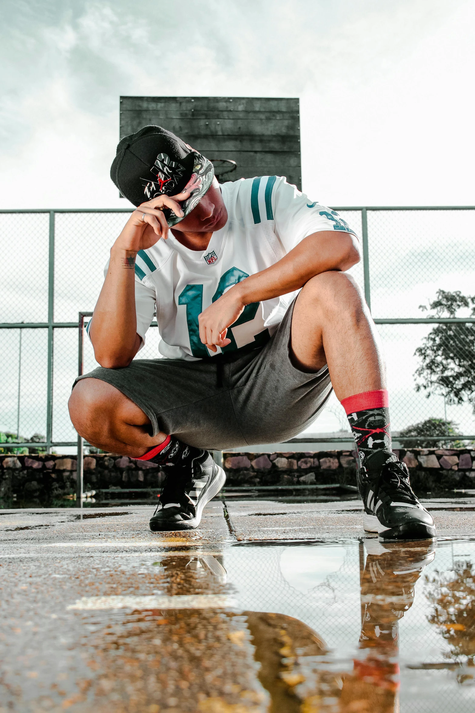 a man squatting down on a basketball court, an album cover, inspired by Eddie Mendoza, unsplash, graffiti, wearing sunglasses and a cap, on a football field, thinking pose, drippy