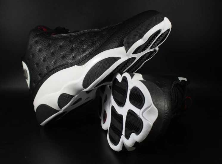 a pair of black and white sneakers on a black background, an album cover, inspired by Jordan Grimmer, trending on dribble, low - angle shot from behind, white with black spots, underside, stacked
