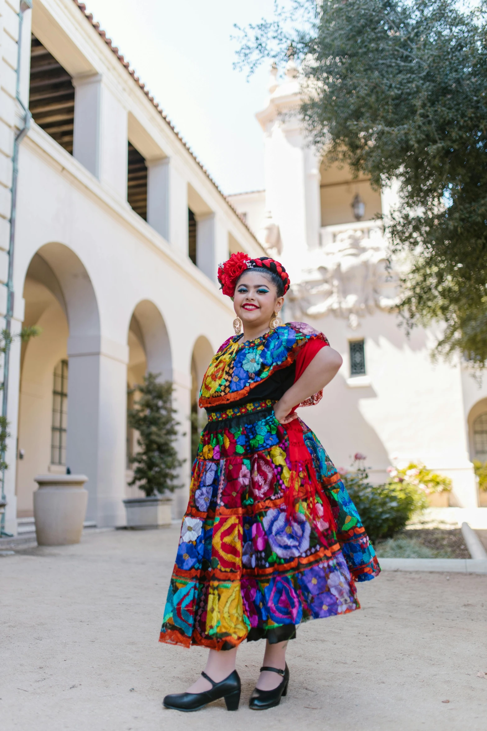 a woman in a colorful dress standing in front of a building, inspired by Frida Kahlo, renaissance, university, recital, square, plus size