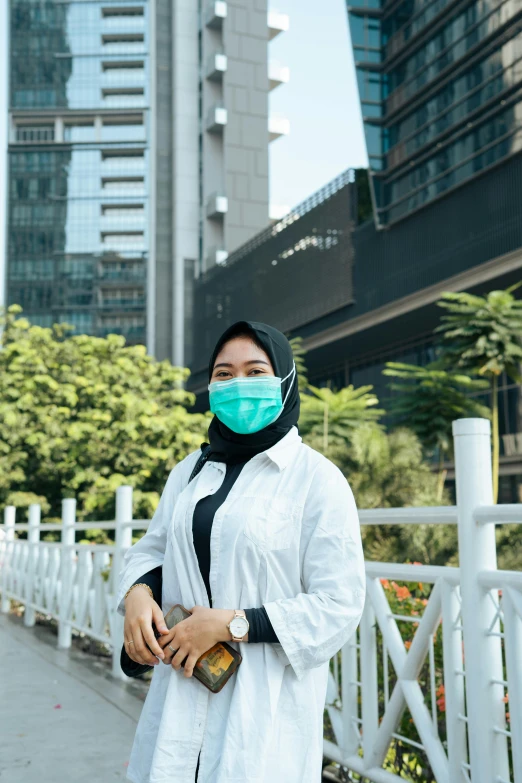 a woman wearing a face mask standing on a sidewalk, by Basuki Abdullah, in a cybercity, sea - green and white clothes, clean medical environment, background image