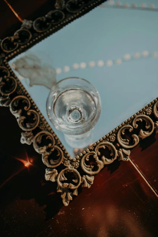 a glass sitting on top of a table next to a mirror, inspired by Elsa Bleda, renaissance, pearl choker, 1 9 2 0's style speakeasy, center of frame, top down shot