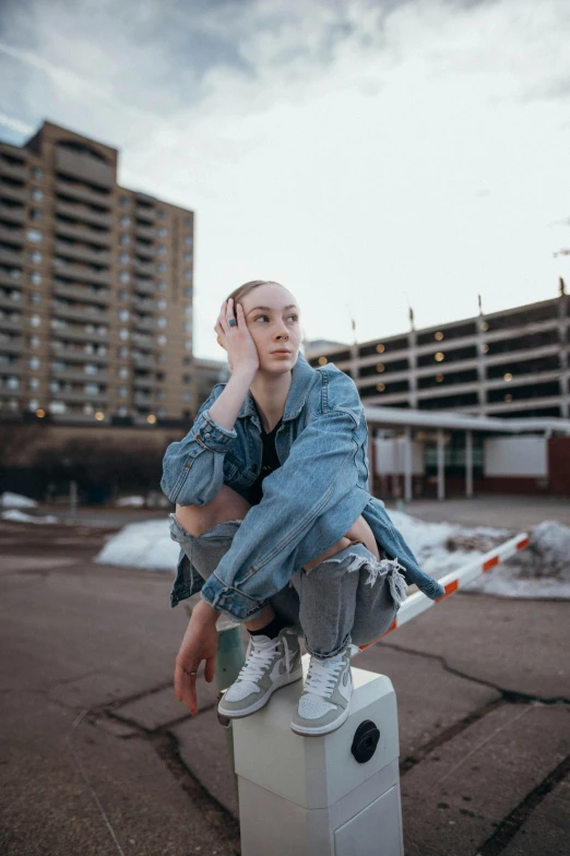 a woman sitting on top of a white box, trending on pexels, hyperrealism, androgynous male, jean jacket, in the city, pale - skinned