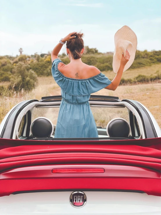 a woman standing in the back of a convertible car, pexels contest winner, renaissance, wearing a red sundress, soft top roof raised, instagram post, back view also