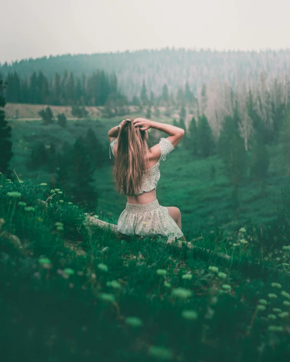 a woman sitting on top of a lush green hillside, inspired by Elsa Bleda, unsplash contest winner, her hair is white, desaturated color, 500px photos, alternate album cover