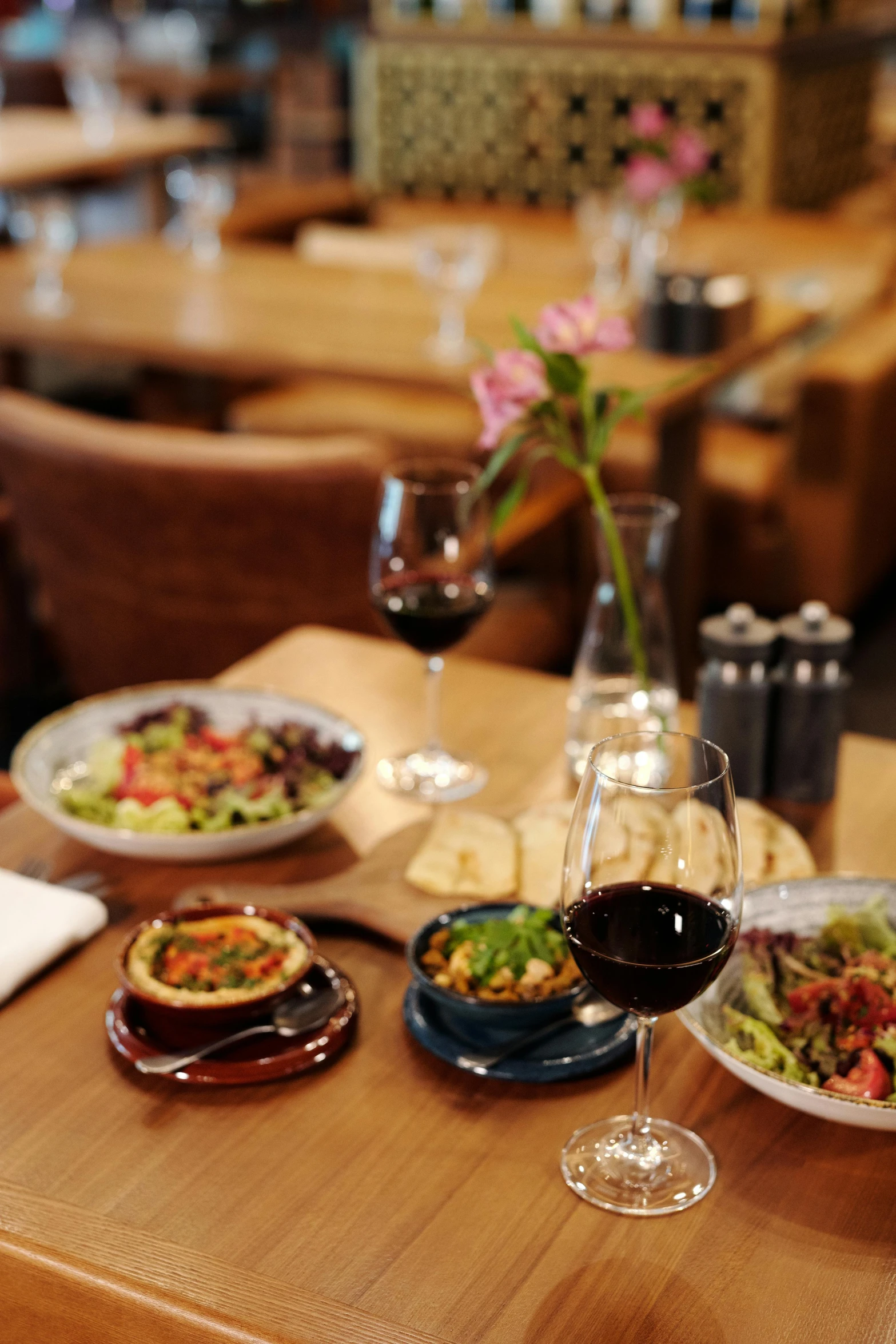 a wooden table topped with plates of food and glasses of wine, bowl filled with food, restaurant, whistler, item