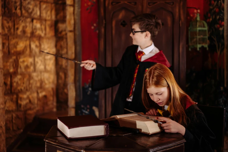 a couple of people that are looking at a book, by Helen Stevenson, pexels contest winner, hogwarts gryffindor common room, magic school uniform, studio photo