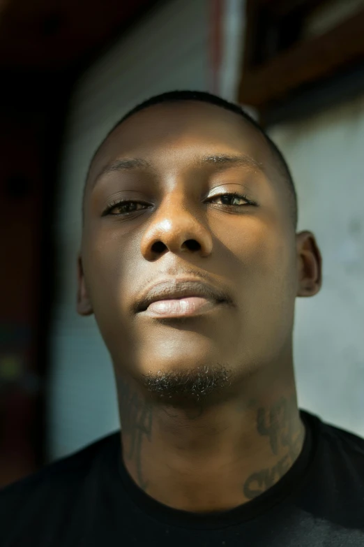 a close up of a person wearing a black shirt, an album cover, inspired by Gregorius Sickinger, bright piercing brown eyes, handsome hip hop young black man, inked, clean shaven wide face