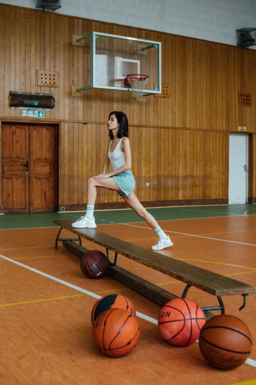a woman standing on top of a bench next to basketballs, by Fei Danxu, dribble, lunging at camera :4, bae suzy, leg high, local gym