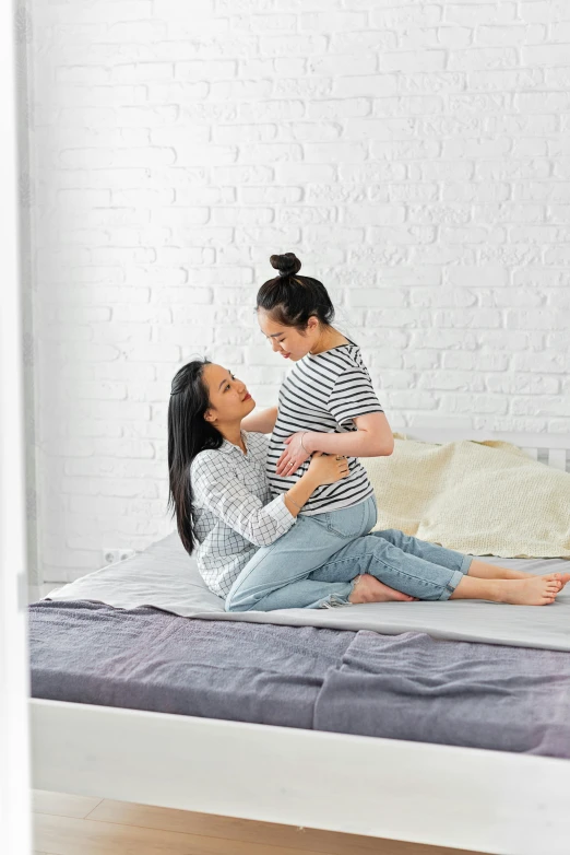 a woman sitting on top of a bed holding a baby, shutterstock contest winner, asian woman, lesbian art, wide full body, instagram post