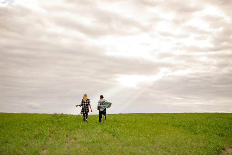 a couple of people standing on top of a lush green field, a picture, by Jessie Algie, unsplash, running towards the camera, plain background, lachlan bailey, people walking into the horizon