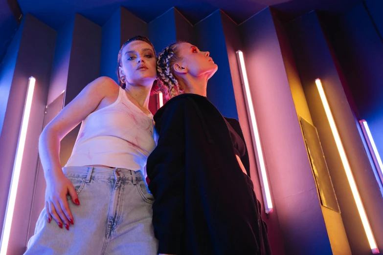 a couple of women standing next to each other, by Matija Jama, trending on pexels, aestheticism, neon lights in the background, fashion studio lighting, promotional image, lightweight