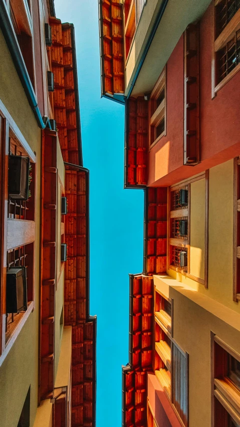 a couple of tall buildings next to each other, inspired by Ricardo Bofill, pexels contest winner, colorful caparisons, nepali architecture buildings, underside, shady alleys