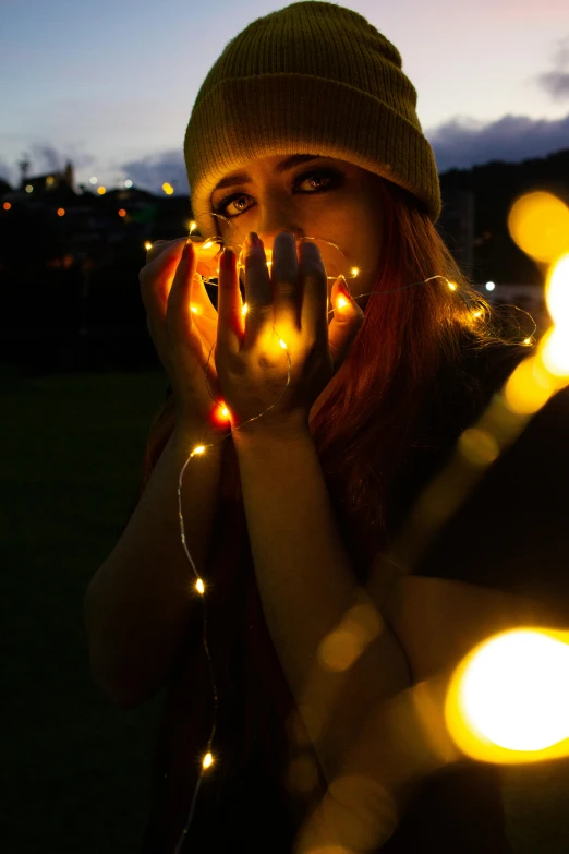 a woman holding a string of lights in front of her face, taken at golden hour, vivid lighting, shot on sony a 7, christmas lights