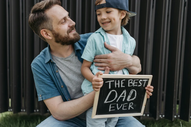 a man holding a sign that says the best dad ever, pexels contest winner, symbolism, avatar image, full frame image, ad image, father with child