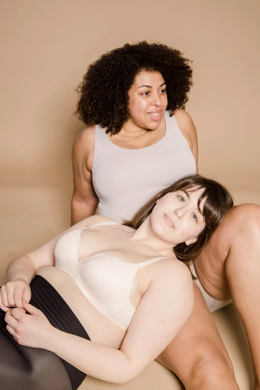 a couple of women sitting on top of a couch, wearing bra, overweight, warm skin tone, someone sits in bed